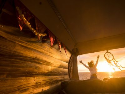 Overjoyed tourist jumping against a golden sunset light viewed from inside a wooden van