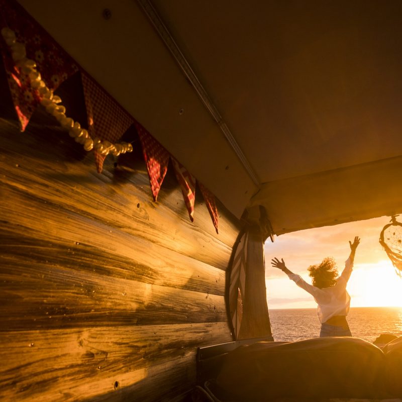 Overjoyed tourist jumping against a golden sunset light viewed from inside a wooden van
